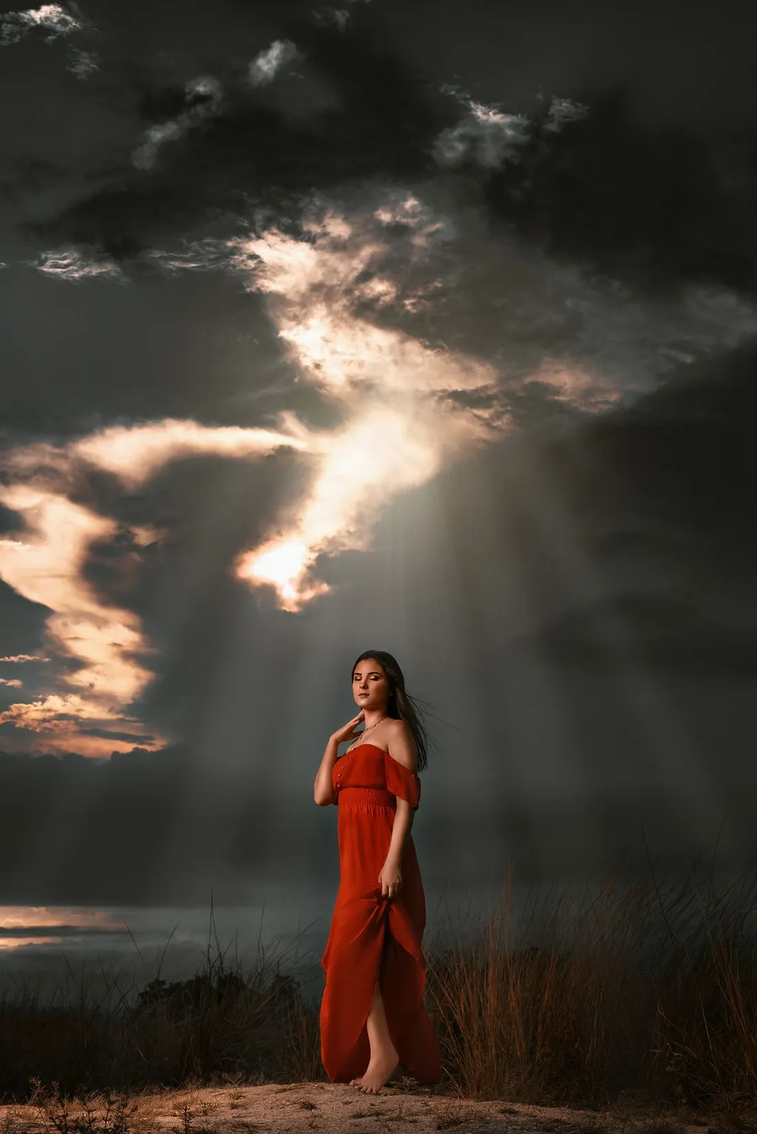 Portrait of a woman in a red dress against a dramatic sunset