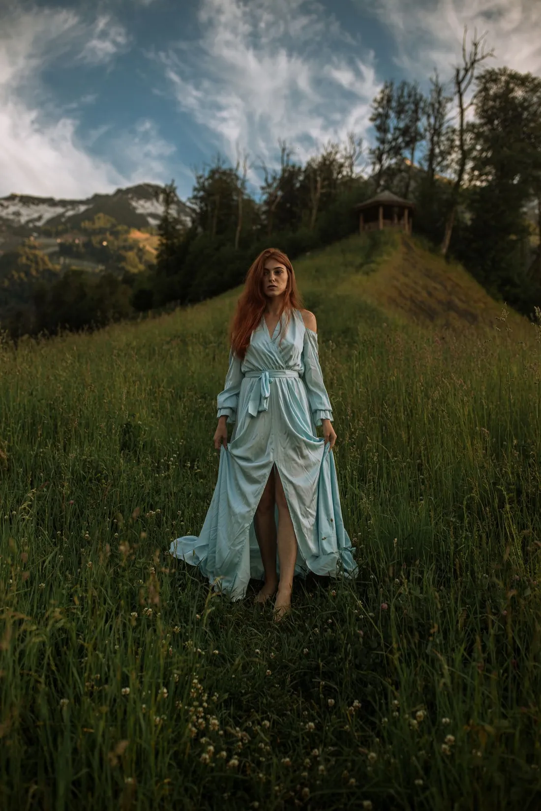 Woman in a long blue dress walking through a green meadow