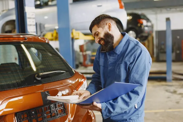 Mechanic with a clipboard checking a car in the workshop